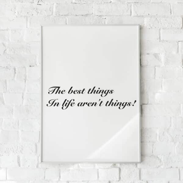 Hvid plakat med sort tekst: “The best things in life aren’t things!”, hængende på hvid murstensvæg.