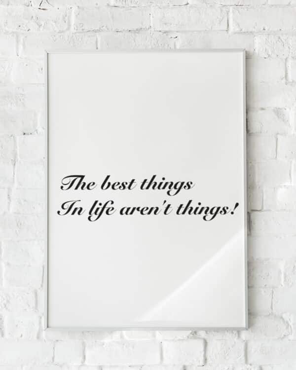 Hvid plakat med sort tekst: “The best things in life aren’t things!”, hængende på hvid murstensvæg.